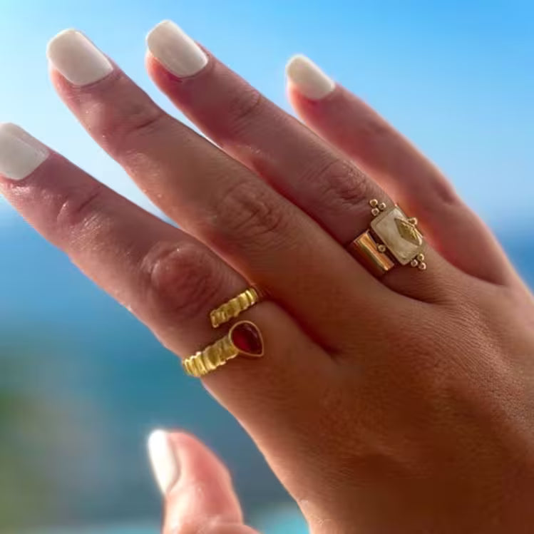 Hand wearing gold rings with a blurred blue sky background