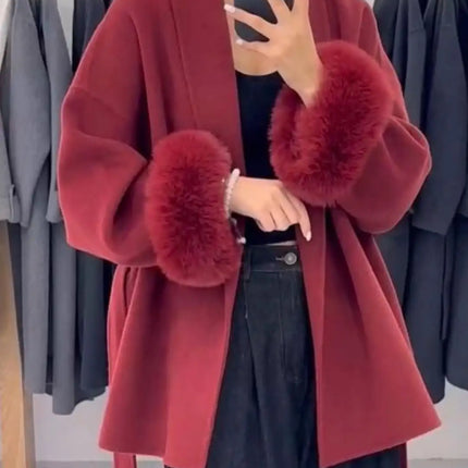 Red coat with fur cuffs worn by a person, with a background of hanging clothes.