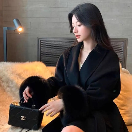 Woman in a black coat holding a black handbag on a yellow couch.