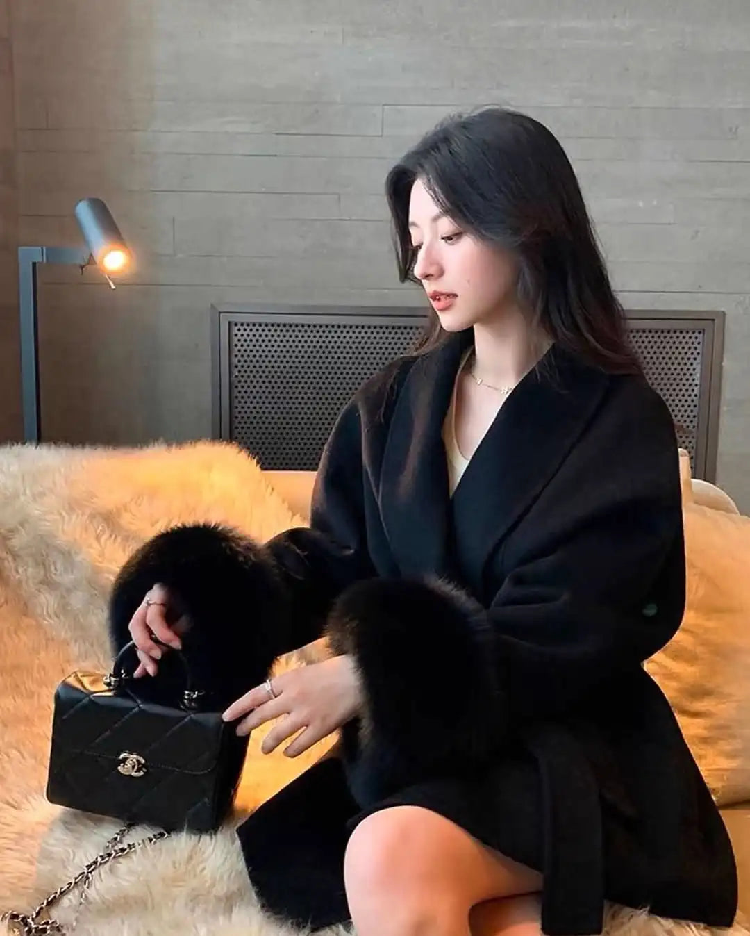 Woman in a black coat holding a black handbag on a yellow couch.