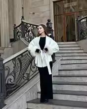 Woman in a white coat standing on a staircase with ornate railings.
