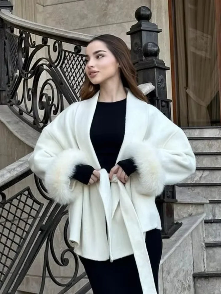 Woman wearing a white coat with fur trim standing on steps.