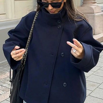 Woman wearing a navy coat and sunglasses, standing on a street.