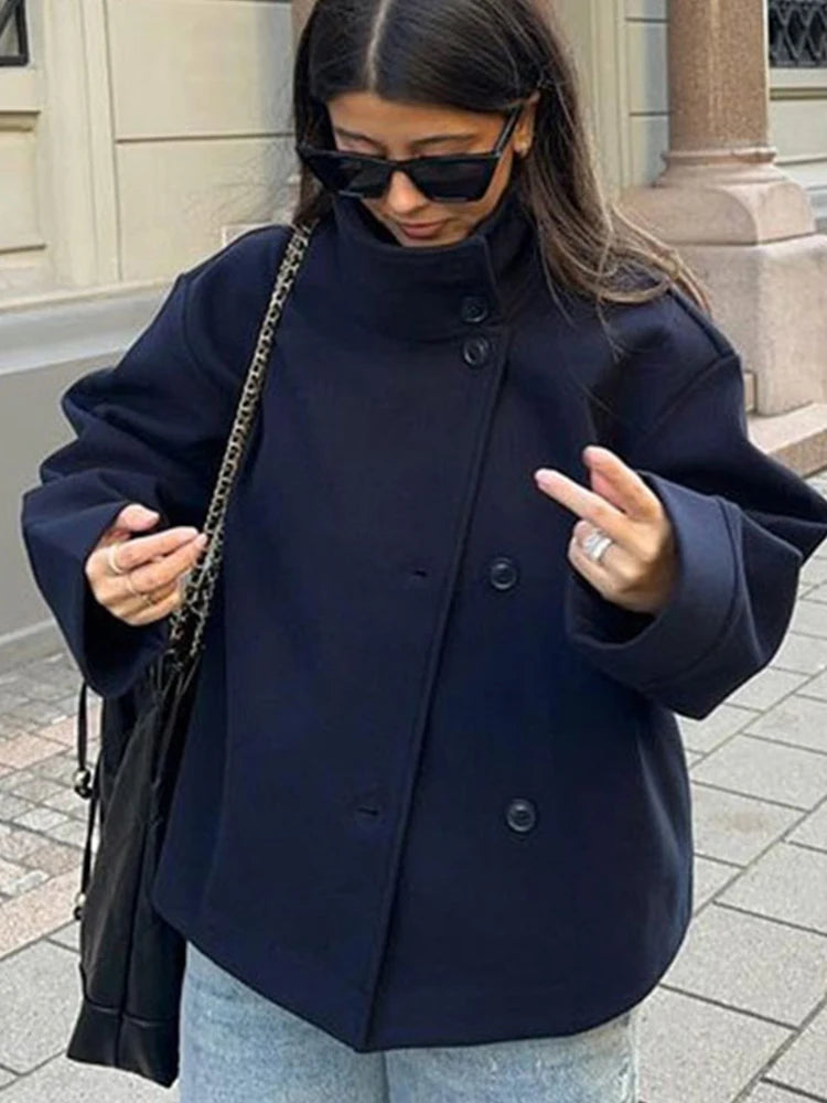 Woman wearing a navy coat and sunglasses, standing on a street.