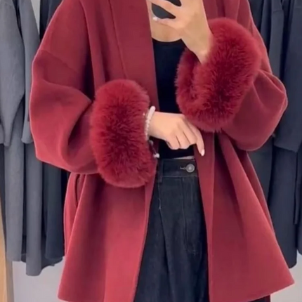 Red coat with fur cuffs worn by a person, standing against a clothing rack.