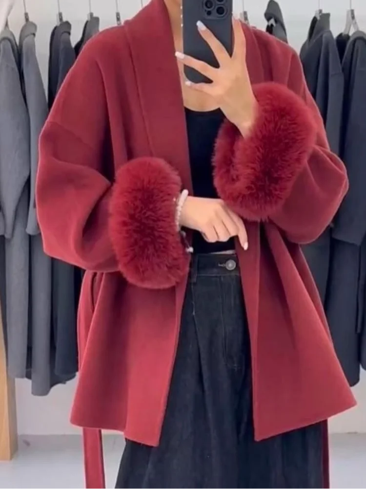 Red coat with fur cuffs worn by a person, standing against a clothing rack.