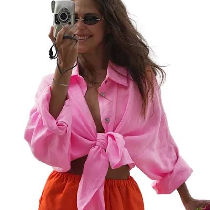Woman wearing a pink shirt and orange pants, holding a camera.