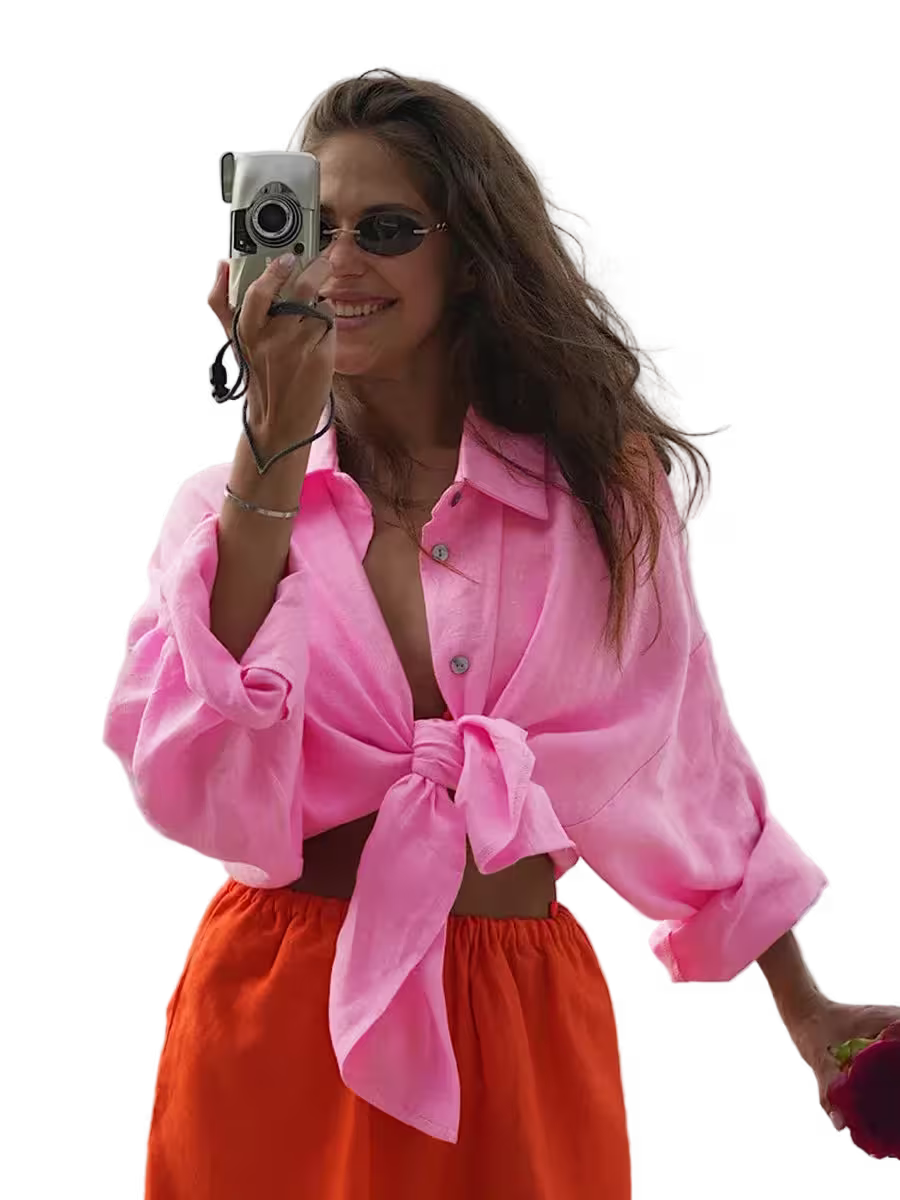 Woman wearing a pink shirt and orange pants, holding a camera.