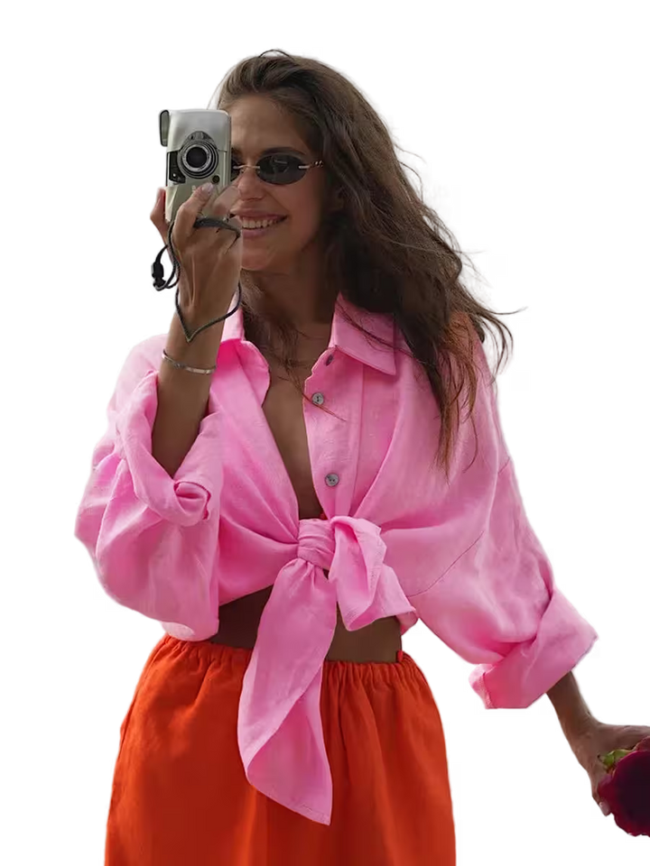 Woman wearing a pink shirt and orange pants, holding a camera.