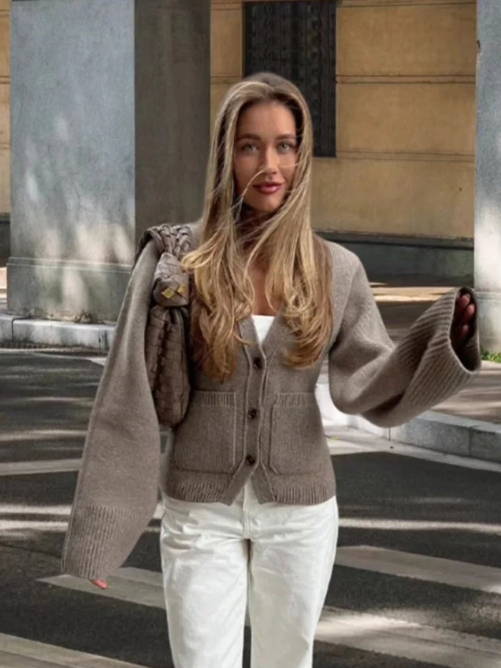 Woman wearing a brown cardigan over a white top and pants, standing outdoors.