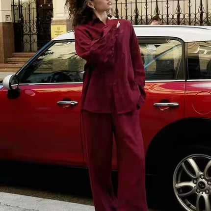 Woman in a burgundy outfit standing next to a red car on a city street.
