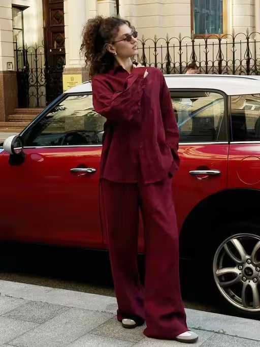 Woman in a burgundy outfit standing next to a red car on a city street.