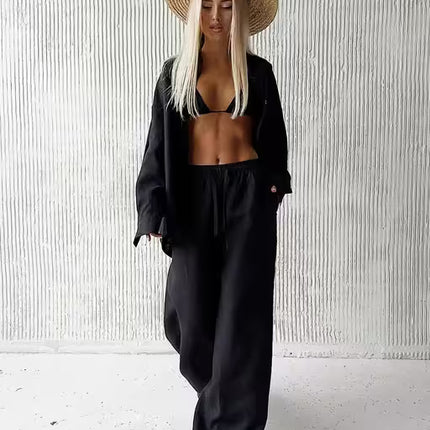 Person wearing a black outfit and straw hat against a white textured wall.