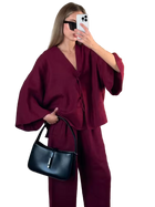 Woman in a burgundy outfit holding a black handbag, taking a mirror selfie.