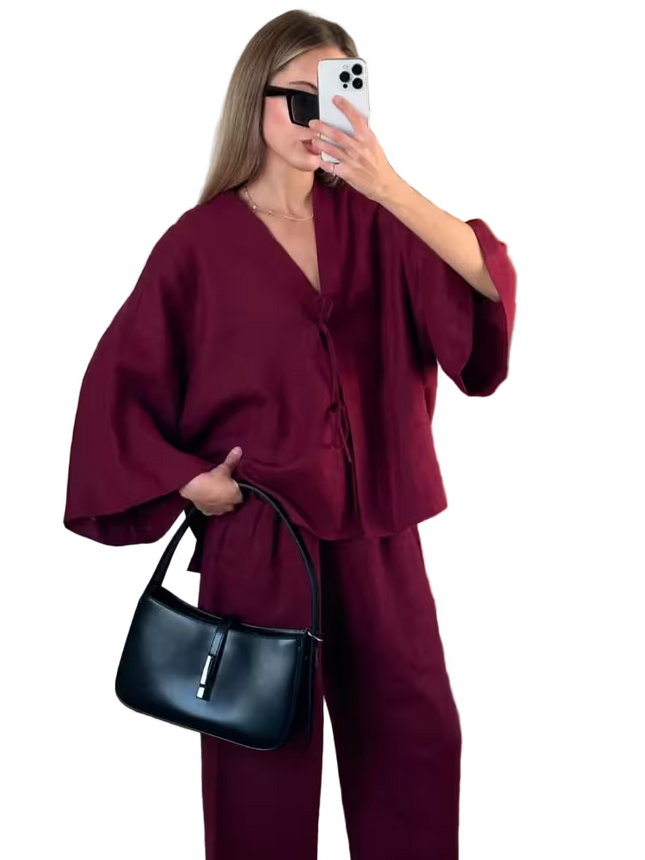 Woman in a burgundy outfit holding a black handbag, taking a mirror selfie.