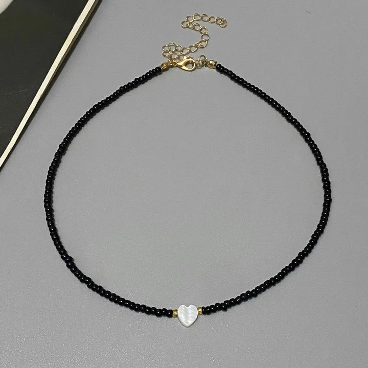 Black beaded necklace with a heart-shaped pendant on a gray surface