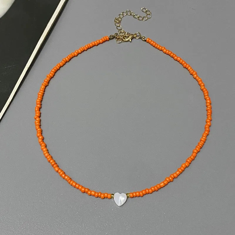 Orange beaded necklace with a silver heart charm on a gray surface