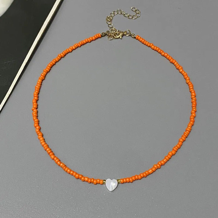 Orange beaded necklace with a silver heart charm on a gray surface