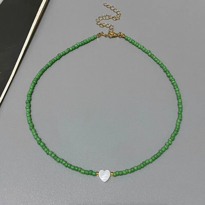 Green beaded necklace with a heart charm on a gray surface