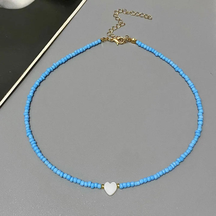 Blue beaded necklace with a heart-shaped charm on a gray surface