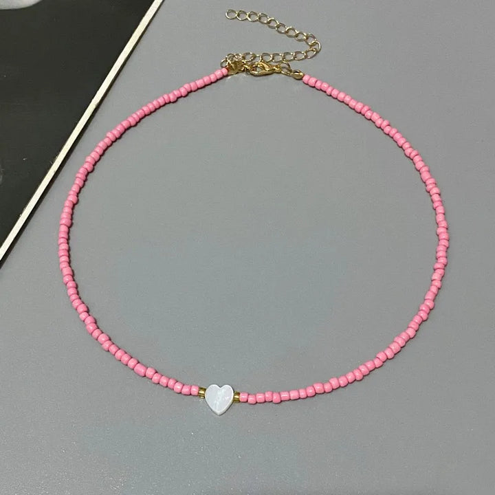 Pink beaded necklace with a heart charm on a gray surface