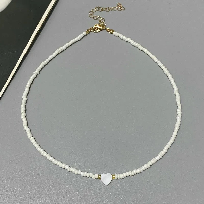 Necklace with white beads and a heart-shaped charm on a gray surface