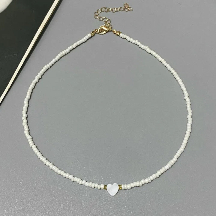 Necklace with white beads and a heart-shaped charm on a gray surface