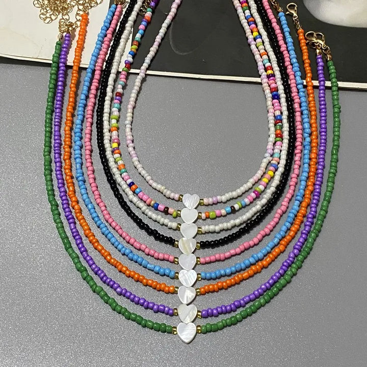 Colorful beaded necklaces with heart-shaped beads on a gray surface