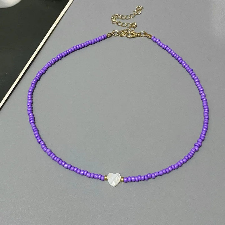Purple beaded necklace with a heart-shaped charm on a gray surface
