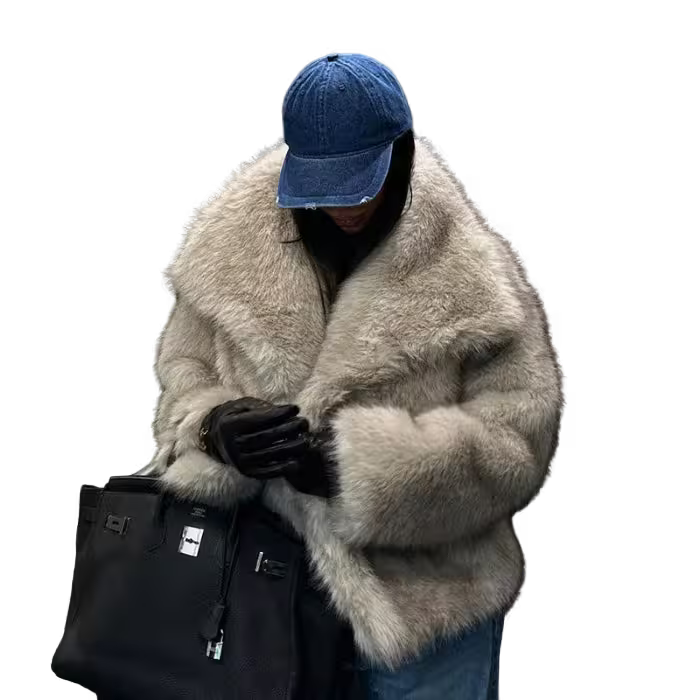 Person wearing a fluffy gray coat, blue cap, and black gloves holding a black bag on a white background