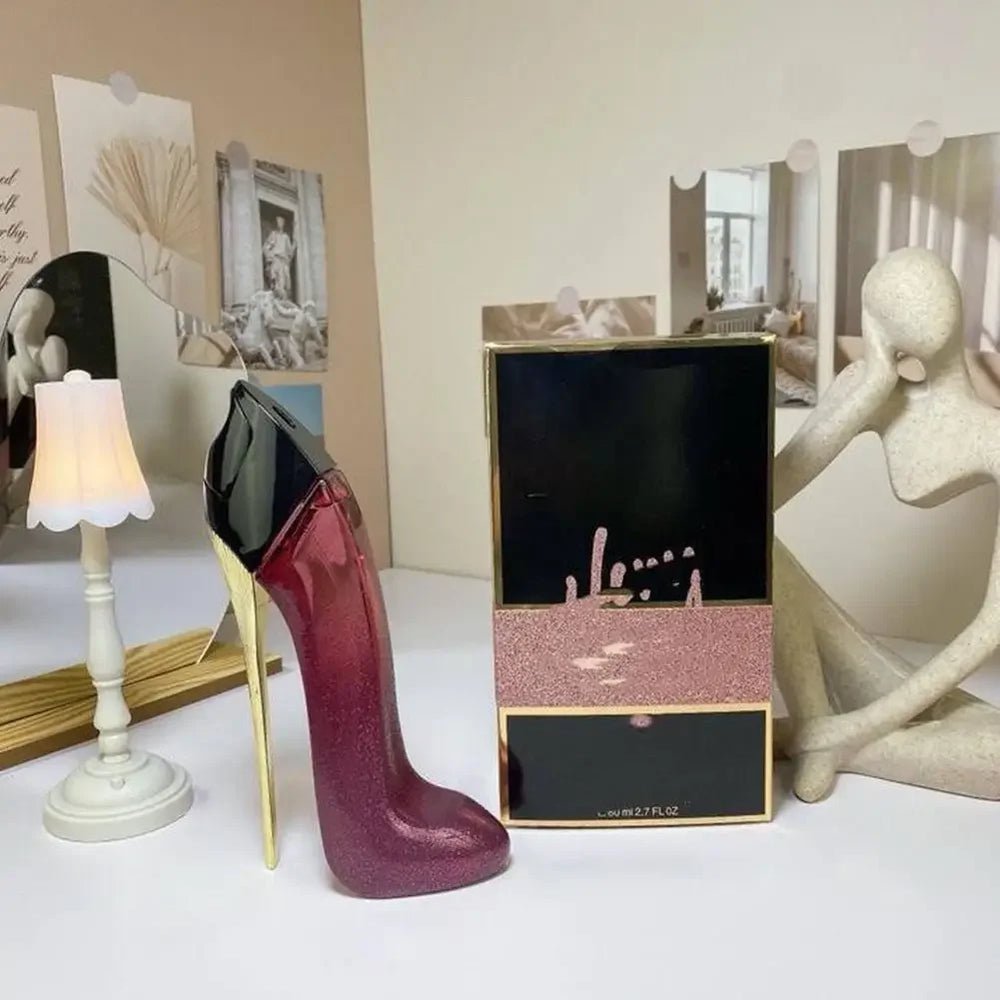 Red high-heeled shoe with gold heel next to a black box on a white surface.