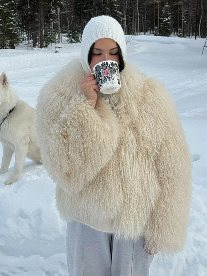 Person in a fluffy white coat holding a mug in a snowy landscape with a dog.