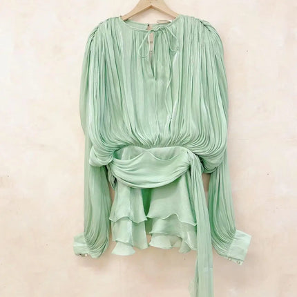 Mint green blouse with long sleeves on a hanger against a light beige background