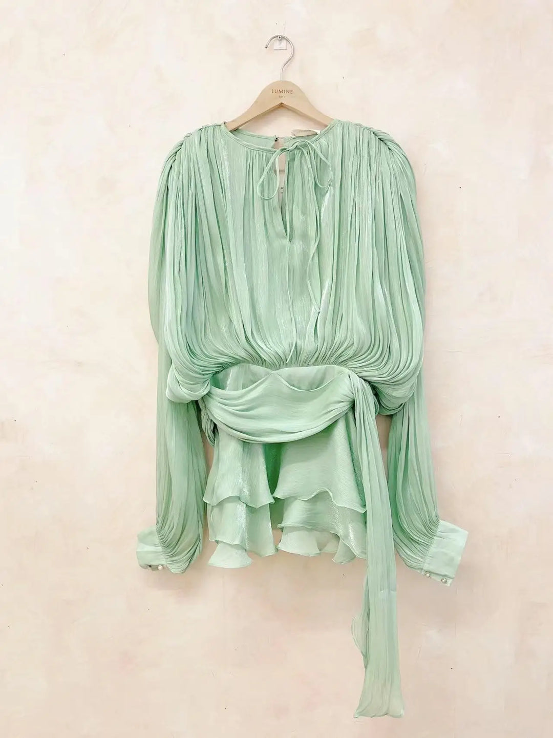 Mint green blouse with long sleeves on a hanger against a light beige background