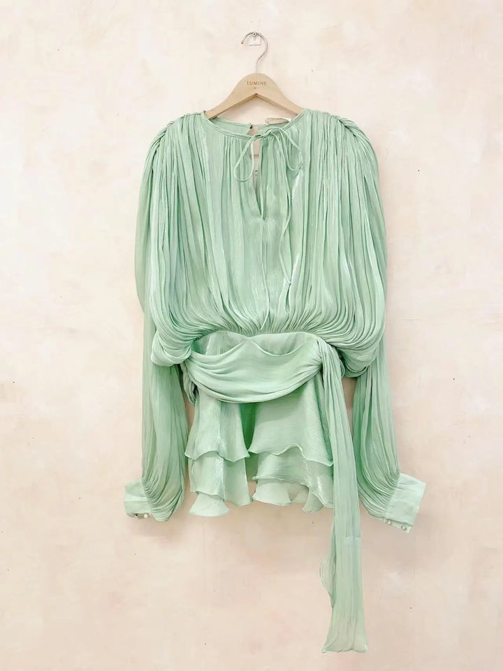 Mint green blouse with long sleeves on a hanger against a light beige background