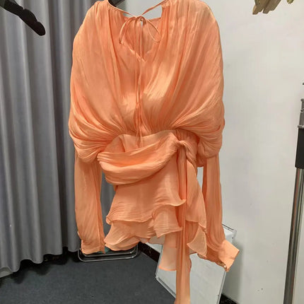 Peach-colored dress on a hanger against a neutral background