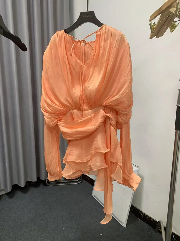 Peach-colored dress on a hanger against a neutral background