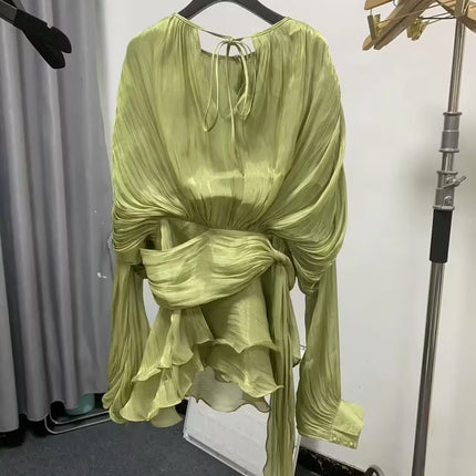 Green dress on a hanger against a white wall with gray curtains.