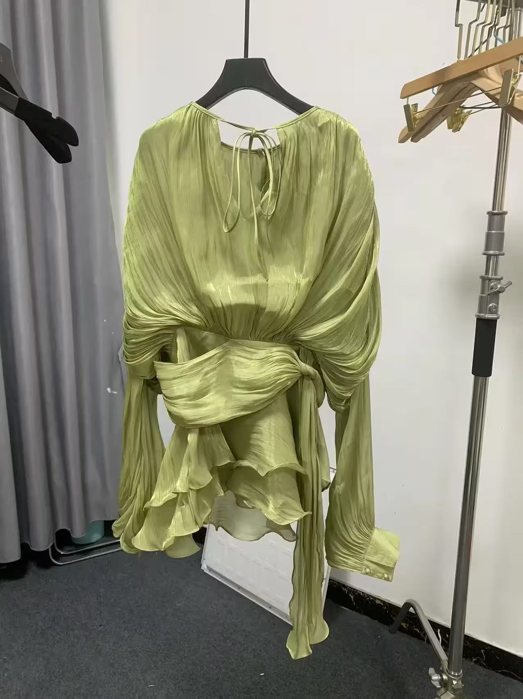 Green dress on a hanger against a white wall with gray curtains.