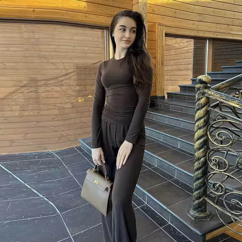 Woman in a brown outfit holding a handbag on a staircase with wooden walls.