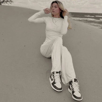 Person sitting on a sandy beach wearing a white outfit and high-top sneakers.