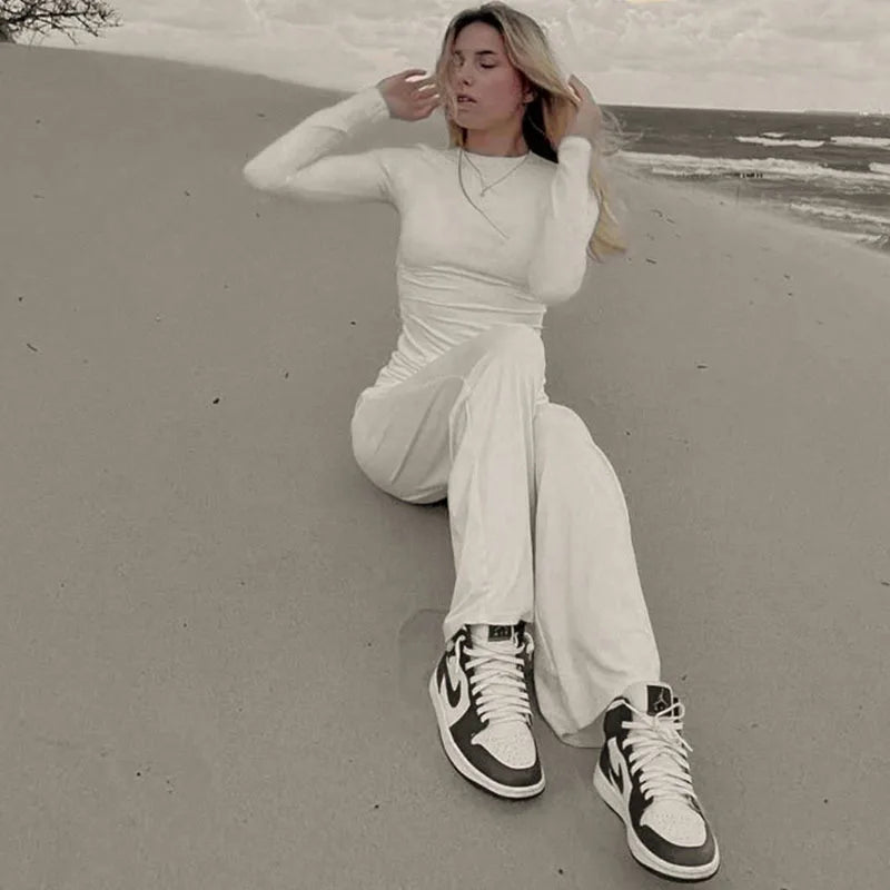 Person sitting on a sandy beach wearing a white outfit and high-top sneakers.