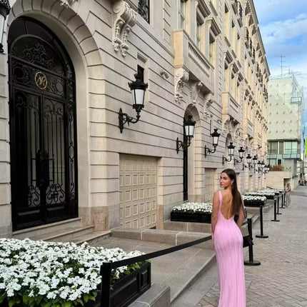 Woman in a pink dress walking past an elegant building with decorative doors and street lamps.