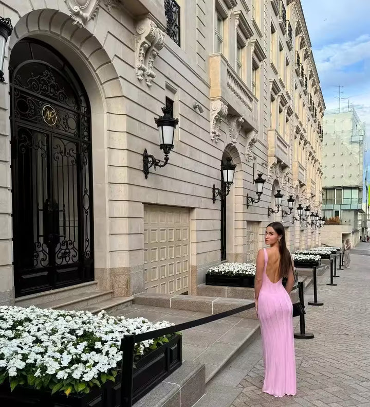Woman in a pink dress walking past an elegant building with decorative doors and street lamps.