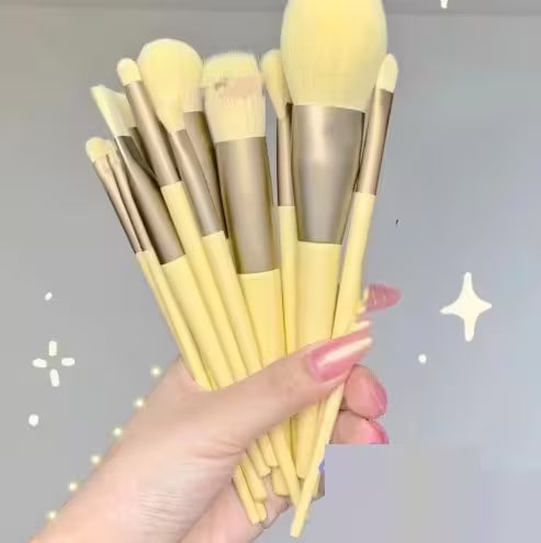Set of yellow makeup brushes held by a hand against a gray background