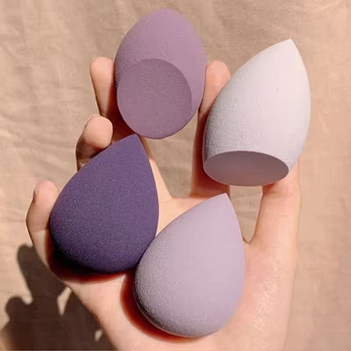 Three purple makeup sponges held in a hand against a beige background