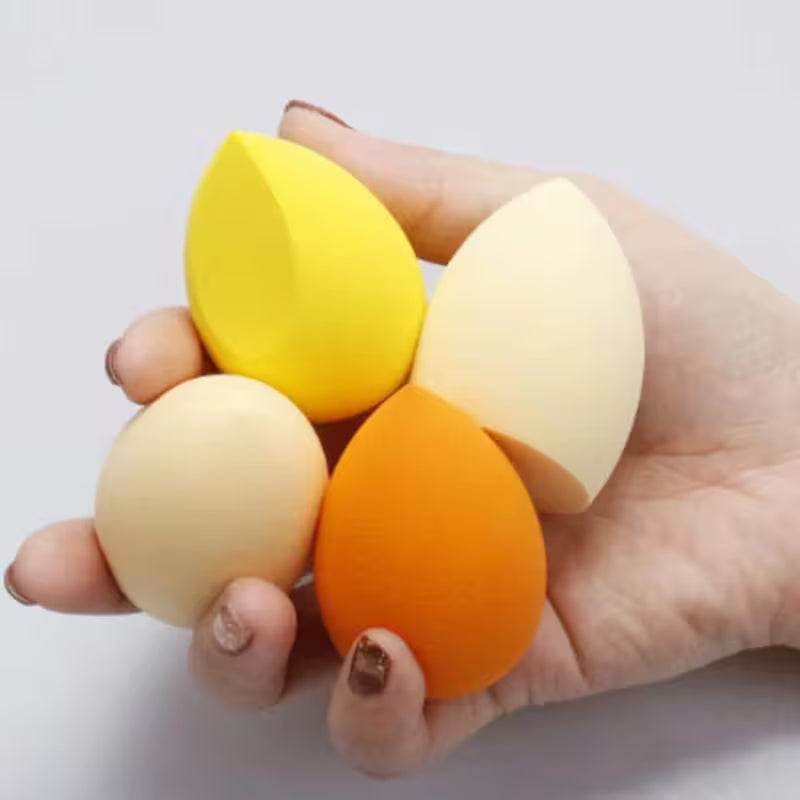 Hand holding four colorful makeup sponges on a white background