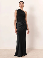 Woman wearing a black one-shoulder gown against a plain background