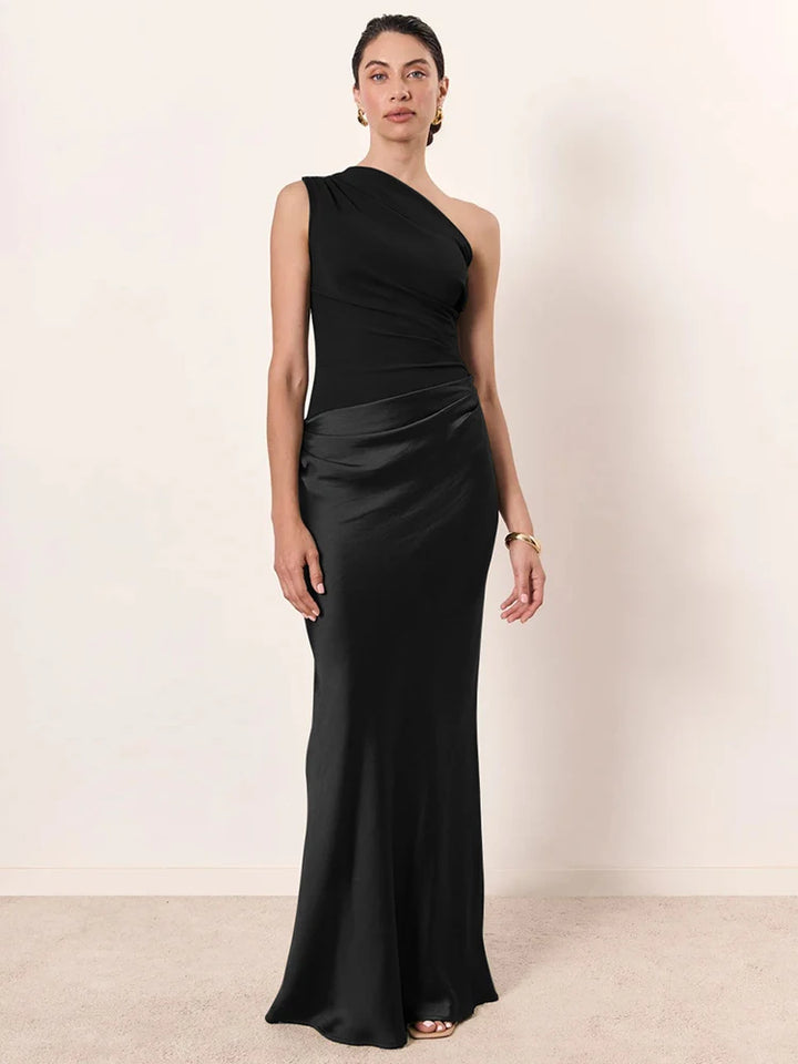 Woman wearing a black one-shoulder gown against a plain background