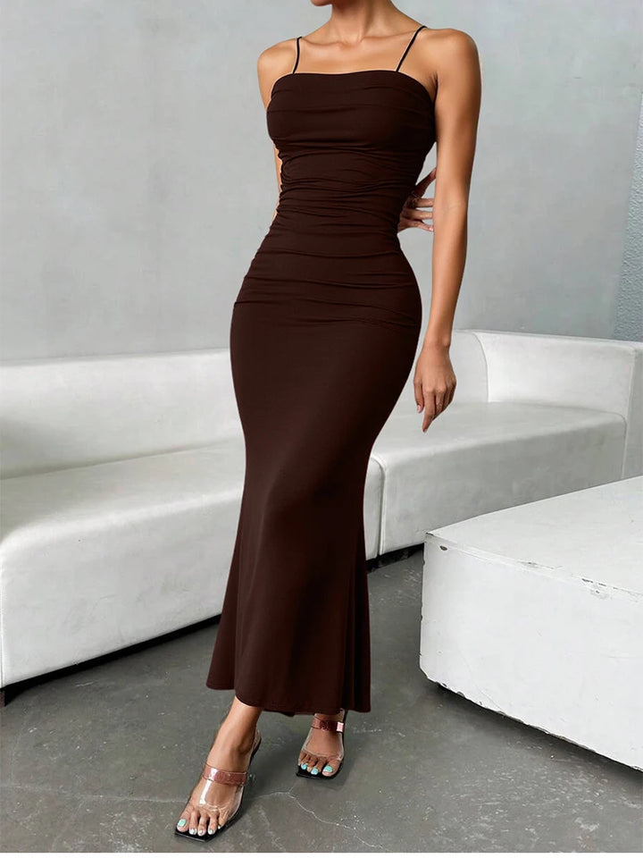 Woman wearing a brown dress standing in a modern indoor setting with white furniture.